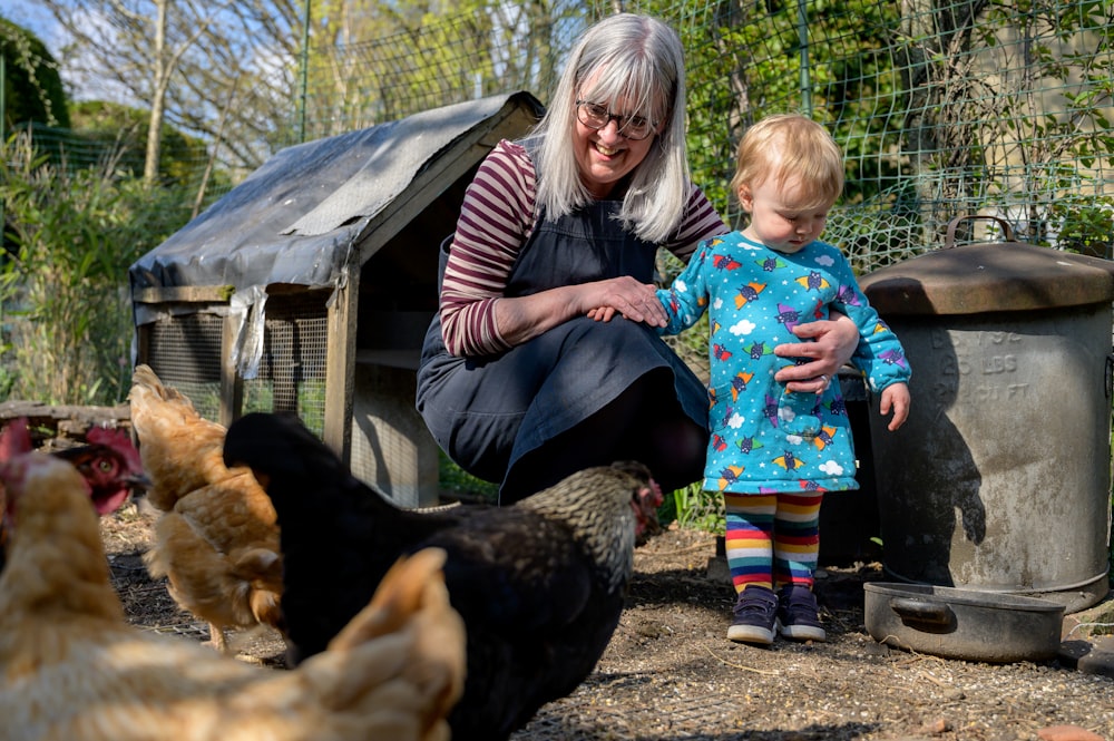 cheerful old woman holding a baby next to chickens
