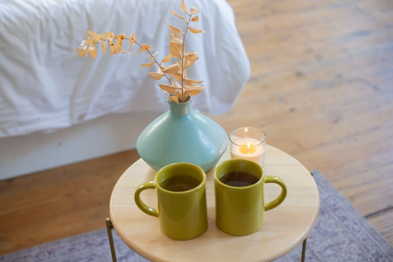 two cups of tea next to a candle and a vase